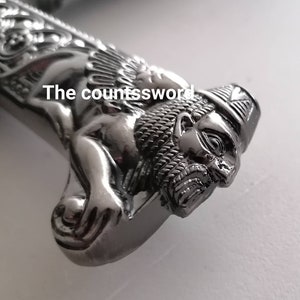 May include: Close-up of a silver sword handle with a lion's head design. The text "The countssword" is visible on the handle. The handle has intricate details and a polished finish.