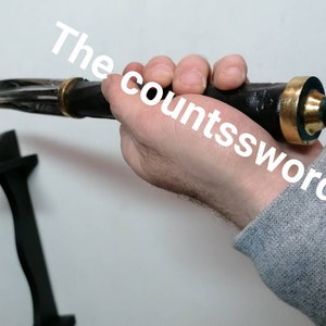 May include: A black and silver dagger with a gold-colored hilt is held in a hand. The dagger has a pointed blade and a black handle. The text "The countssword" is visible in the image.