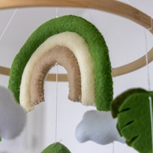 May include: A wooden ring with a green, white, and brown felt rainbow hanging from it. There are also felt clouds and a green felt leaf hanging from the ring.