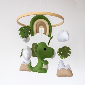 May include: A green felt dinosaur mobile with a rainbow, clouds, and palm leaves hanging from a wooden ring.