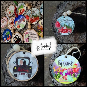 May include: A collection of personalized Christmas ornaments with various designs. Some ornaments feature names like "Nathan" and "Brooks," while others display text such as "My 1st Christmas." Designs include a red truck, a dinosaur in a Santa hat, and a family in a car.