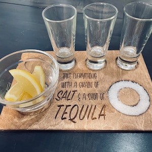 May include: Wooden serving tray with three shot glasses, a small bowl with lemon slices, and a circle of salt. The tray has the text "Take everything with a grain of salt & a shot of tequila" engraved on it.