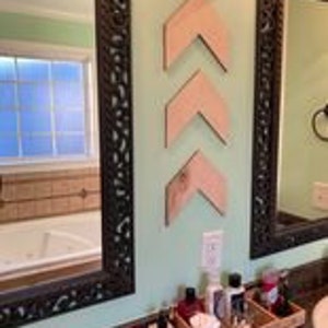 Puede incluir: Tres piezas de decoración de pared de madera en forma de chevron en un tono de madera claro, dispuestas verticalmente en un patrón escalonado en una pared verde claro.