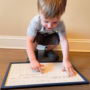 May include: A child is pointing at a chart with the letters of the alphabet and numbers. The chart is titled "You did it! My name is ILANDON".