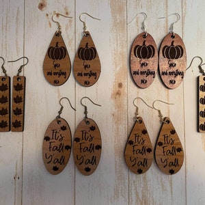 Puede incluir: Surtido de pendientes de madera con diseños de otoño. Los pendientes presentan calabazas, hojas y el texto "It's Fall Y'all".