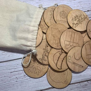 May include: A beige drawstring bag with wooden Christmas ornaments spilling out. The ornaments are round with etched designs of a Christmas tree, snowflake, gifts, and the words "Merry Christmas".