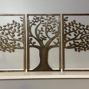 Może przedstawiać: Trzyczęściowa drewniana sztuka ścienna z motywem drzewa. Każdy element ma ciemnobrązową ramę z wyciętym wzorem drzewa i liści. Tło jest białe, a grafika jest prezentowana na białej powierzchni.