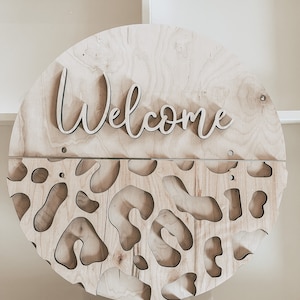 May include: A round wooden sign with the word "Welcome" cut out in a script font. The bottom half of the sign features a leopard print pattern.