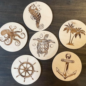 May include: Six round wooden coasters with different sea-themed designs. The coasters feature a seahorse, octopus, turtle, palm trees, anchor, and a ship's wheel.