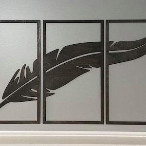 May include: Three wooden frames with a black feather design cut out. The frames are arranged horizontally and the feather design is continuous across all three frames.