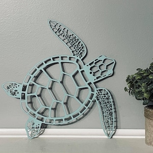 May include: A light blue metal sea turtle wall decor with a detailed cutout design. The turtle is facing right and has a long neck and tail.