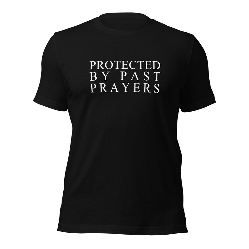 Op de afbeelding: Zwart T-shirt met witte tekst die "PROTECTED BY PAST PRAYERS" luidt.
