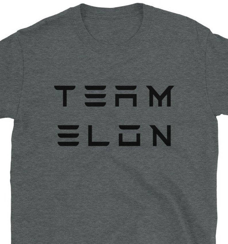 Op de afbeelding: Een heidekleurig T-shirt met de tekst "TEAM ELON" in zwart gedrukt.