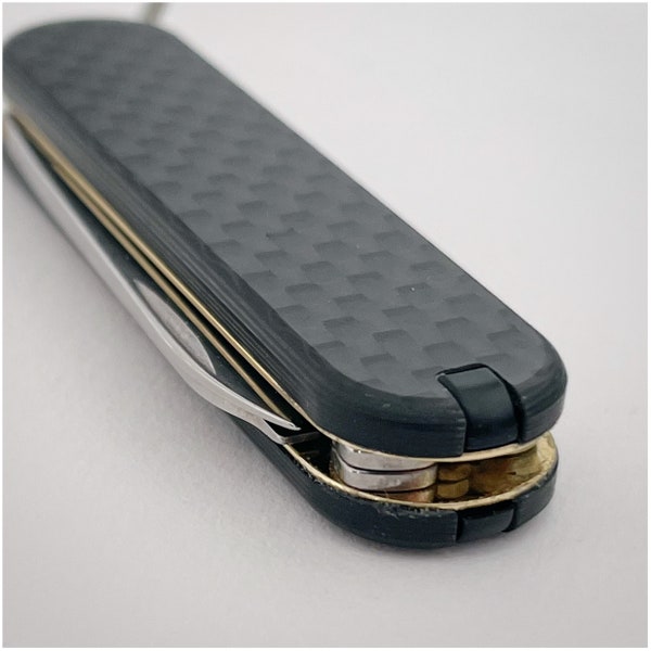 Victorinox Classic pocketknife with brass liners, carbonfiber-scales and black accessories.