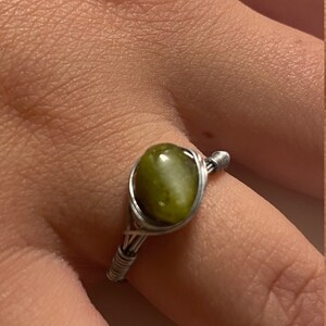 May include: A silver wire wrapped ring with a green gemstone. The ring is on a finger.