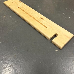 May include: A wooden bath caddy with a long, rectangular shape and a cut-out for a soap dish. The caddy has a hole for a bottle and a groove for a bar of soap.