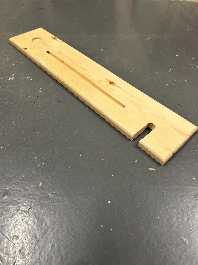 May include: A wooden bath caddy with a long, rectangular shape and a cut-out for a soap dish. The caddy has a hole for a bottle and a groove for a bar of soap.