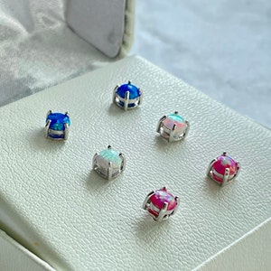 May include: Five pairs of opal earrings in a white box. The earrings are in a variety of colors, including blue, white, and pink.