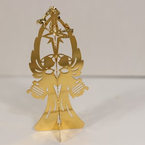 May include: Gold-colored metal Christmas ornament featuring two angels with wings, holding musical instruments, standing under a star.