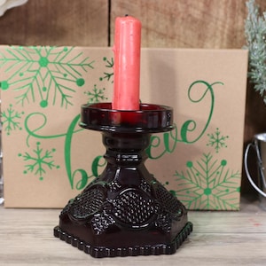 May include: A dark red glass candle holder with a decorative design. A red candle is in the holder.