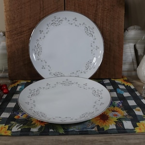May include: Two white ceramic dinner plates with a silver rim and a delicate floral pattern. The plates are stacked on top of each other.