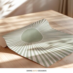 Puede incluir: Un rollo de papel tapiz a rayas verdes y blancas con un c&iacute;rculo verde grande en el centro. El papel tapiz est&aacute; enrollado sobre una superficie de madera. Daring Dutch Designers est&aacute; impreso en la parte inferior de la imagen.