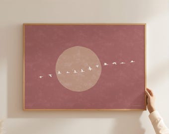 May include: A rectangular wall art print in a wooden frame featuring a dusty rose background with a large, pale beige circular shape in the center. A horizontal line of small, white, stylized birds in flight crosses the center of the circle.
