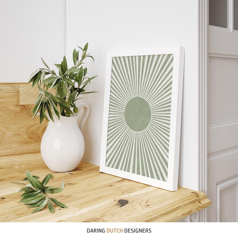 Puede incluir: Una impresi&oacute;n enmarcada en blanco con un dise&ntilde;o de rayos de sol verde y blanco. La impresi&oacute;n est&aacute; sobre una superficie de madera junto a una jarra blanca con hojas verdes.