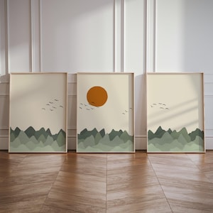 Peut inclure: Trois impressions d'art encadrées représentant des paysages minimalistes. Chaque œuvre présente une chaîne de montagnes vertes, un ciel beige et un vol d'oiseaux noirs. L'impression centrale inclut un grand soleil orange.