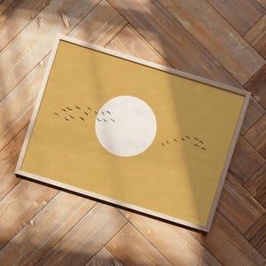Może przedstawiać: Oprawiony wydruk artystyczny o minimalistycznym designie. Grafika przedstawia duży, białawy okrąg reprezentujący słońce, na musztardowożółtym tle. Sylwetki ptaków lecą przed słońcem. Rama jest w jasnym kolorze drewna.