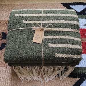 May include: A green and white striped woven blanket with fringe, tied with twine and a brown tag that reads "SW BLANKET CO."