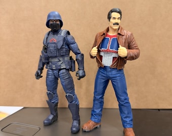 May include: Two action figures standing side by side. The left figure wears a dark blue tactical uniform with a helmet and face mask. The right figure has a moustache, wearing a brown leather jacket over a red and blue chest piece with blue jeans.