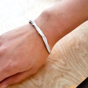 May include: A silver twisted bangle bracelet. The bracelet is made of a thick, twisted wire and has a polished finish.