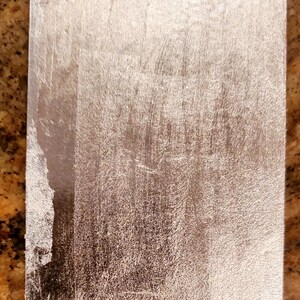 May include: A silver metal plate with a brushed finish. The plate has a slightly rounded edge and a smooth surface.