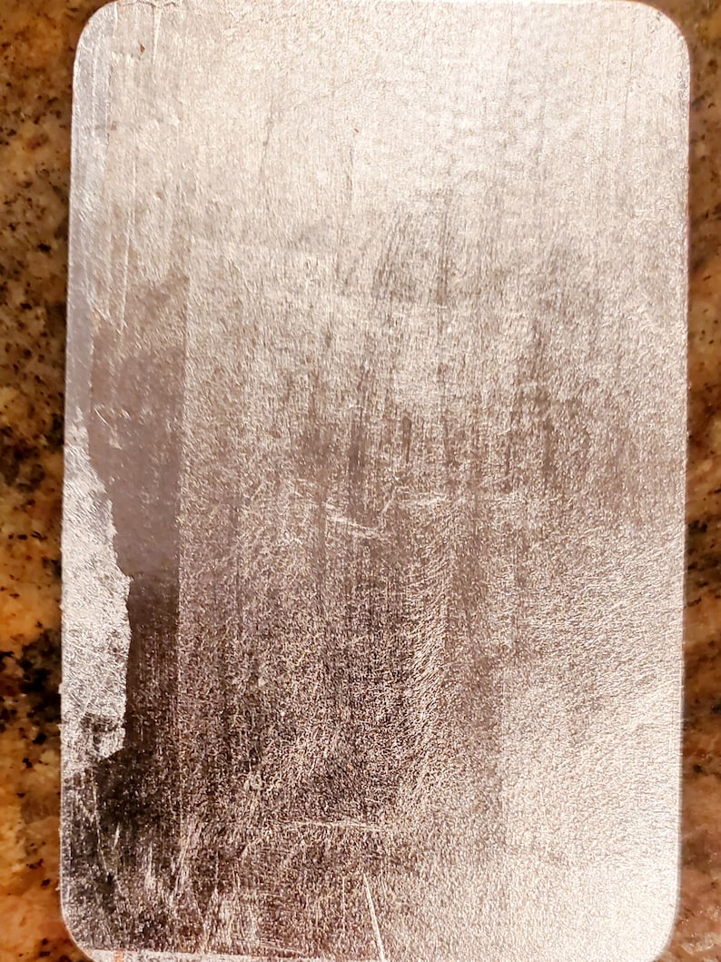 May include: A silver metal plate with a brushed finish. The plate has a slightly rounded edge and a smooth surface.