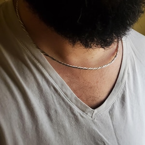 May include: A silver twisted rope chain necklace on a person's neck.