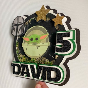 May include: A green and black cake topper featuring a character from the Star Wars franchise, a number 5, and the name "DAVID".