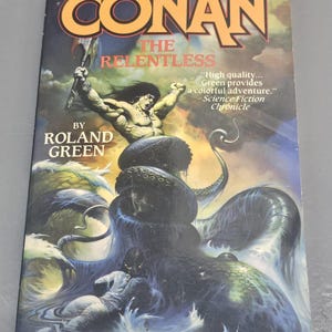 May include: A book cover featuring a muscular man with a sword fighting a large, dark blue octopus. The title of the book is "Conan The Relentless" by Roland Green. The text "High quality... Green provides a colorful adventure." is printed on the cover.