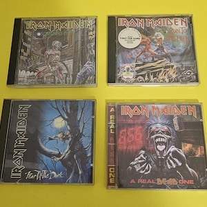 May include: Four Iron Maiden CD albums. The album covers feature illustrations of a skeletal figure, a battle scene, a creature in a dark forest, and a zombie-like figure. The CDs are in clear plastic cases.