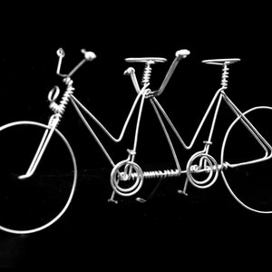 Könnte beinhalten: Eine silberne Draht-Skulptur eines Tandems. Das Fahrrad hat zwei Räder, einen Lenker und einen Sattel.