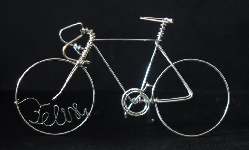 Puede incluir: Una escultura de bicicleta de alambre plateado con el nombre "Felix" escrito en la llanta delantera.