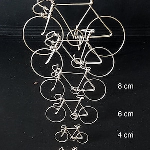 Puede incluir: Cinco bicicletas de alambre plateado de diferentes tama&ntilde;os, que van de 3 a 8 cent&iacute;metros de altura. Las bicicletas est&aacute;n dispuestas en una pila vertical, con la m&aacute;s grande en la parte superior y la m&aacute;s peque&ntilde;a en la parte inferior.
