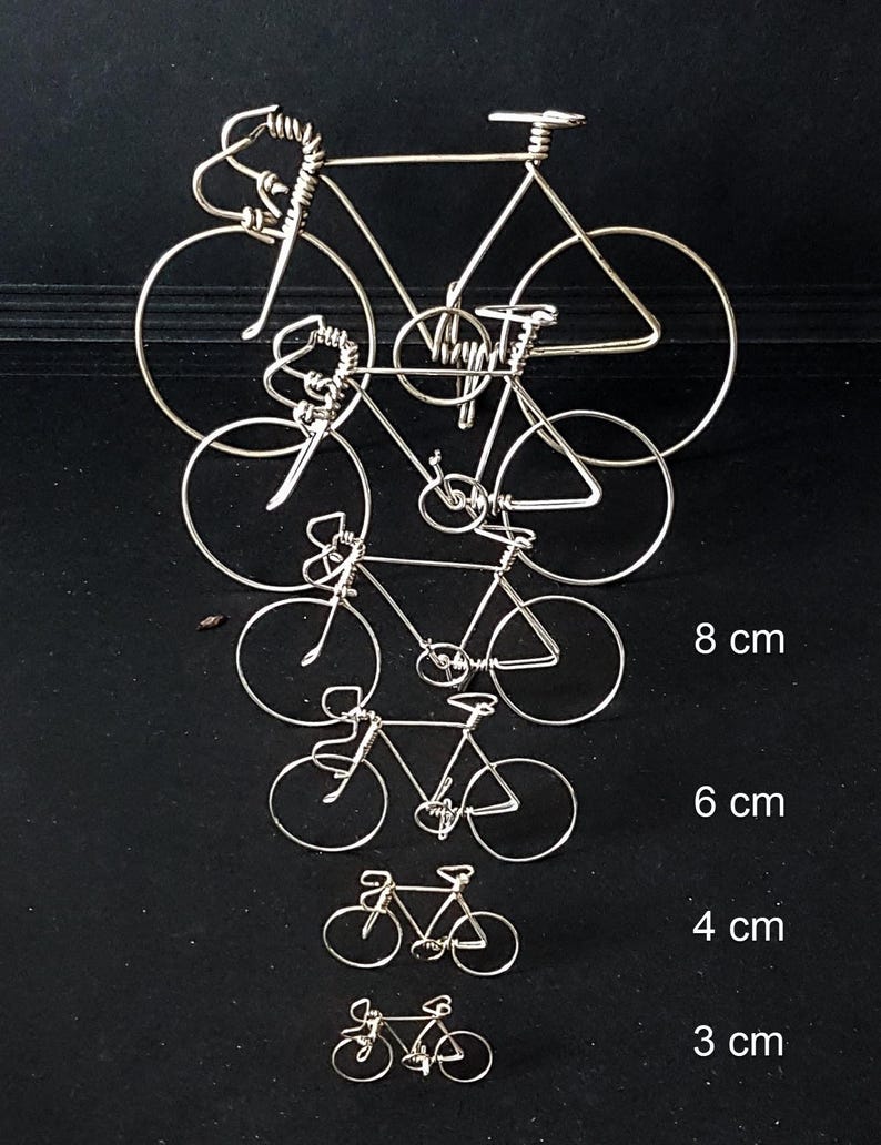 Puede incluir: Cinco bicicletas de alambre plateado de diferentes tama&ntilde;os, que van de 3 a 8 cent&iacute;metros de altura. Las bicicletas est&aacute;n dispuestas en una pila vertical, con la m&aacute;s grande en la parte superior y la m&aacute;s peque&ntilde;a en la parte inferior.