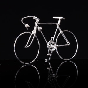 Puede incluir: Una escultura de bicicleta de alambre plateado con ruedas finas y un marco detallado.