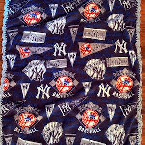 May include: A navy blue fleece blanket with a repeating pattern of New York Yankees logos, baseballs, and pennants. The blanket has a light blue crocheted border. The text "New York Yankees Baseball" is visible throughout the design.