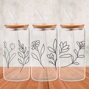 May include: Three clear glass water bottles with bamboo lids and black floral designs. Each bottle has a reusable straw.