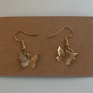 May include: A pair of gold butterfly earrings with a delicate design. The earrings are on a brown background.