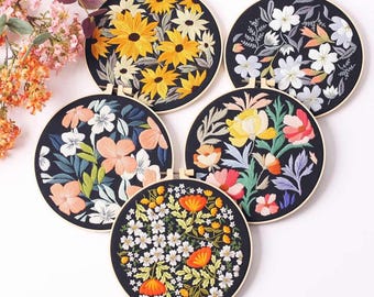 May include: Five embroidery hoops with black fabric and colorful floral embroidery designs. The designs include sunflowers, small white flowers, large pink flowers, red poppies, and a mix of colorful flowers.