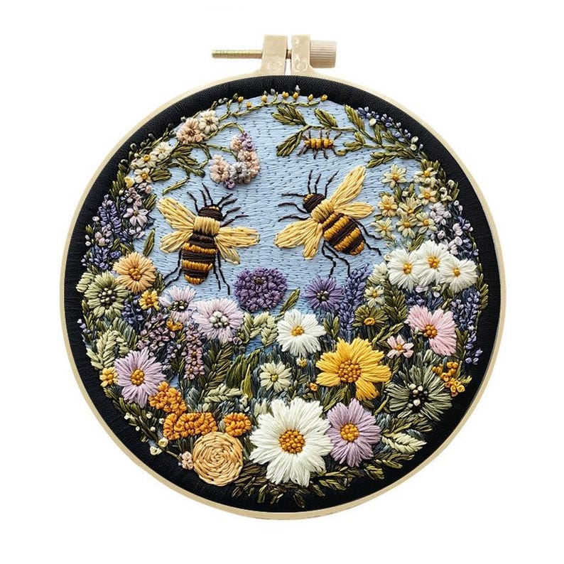 May include: Embroidered hoop art featuring two bees and various flowers in shades of yellow, white, purple, and orange. The bees have brown and yellow stripes. The background is light blue, and the hoop is black.