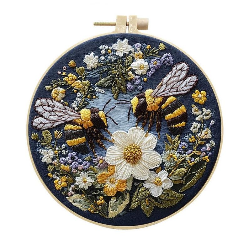 May include: Embroidered hoop art featuring two bumblebees surrounded by colorful flowers. The bees have black and yellow stripes, with detailed wings. The flowers include white daisies, yellow blooms, and purple accents, all set against a dark blue background.